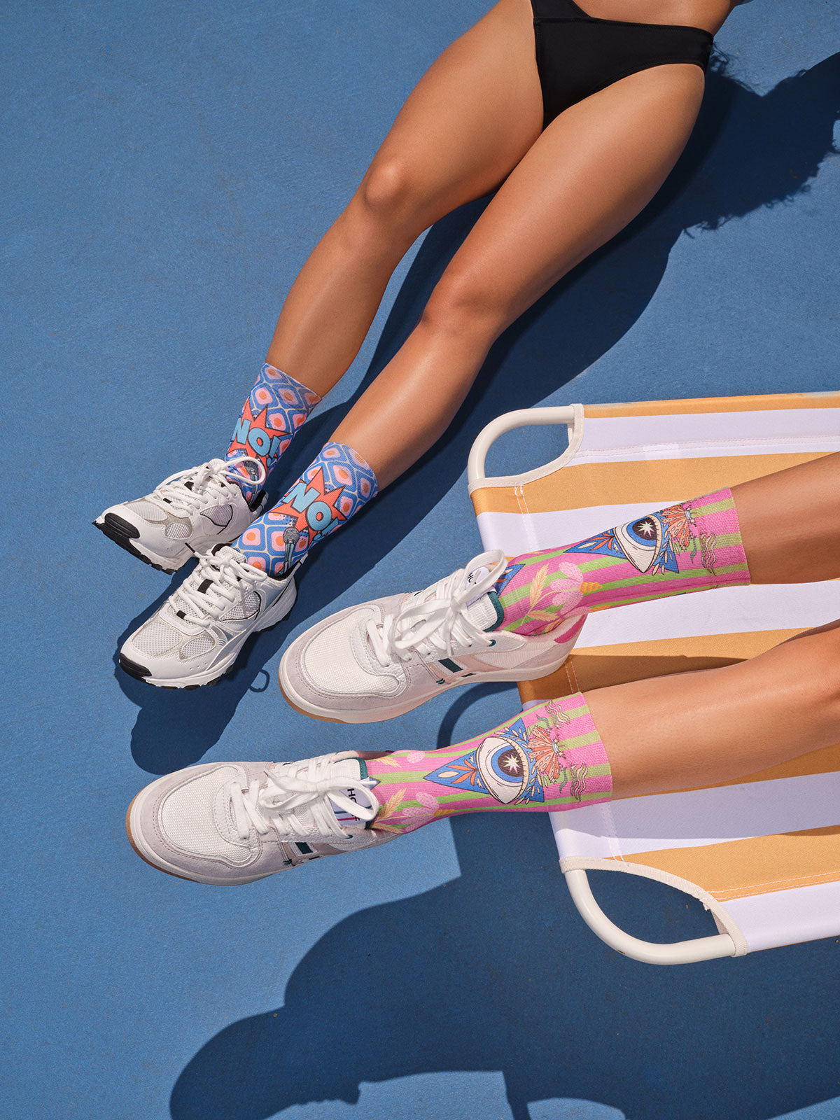 Two pairs of legs wearing colourful socks on a blue surface with a chair in the background.