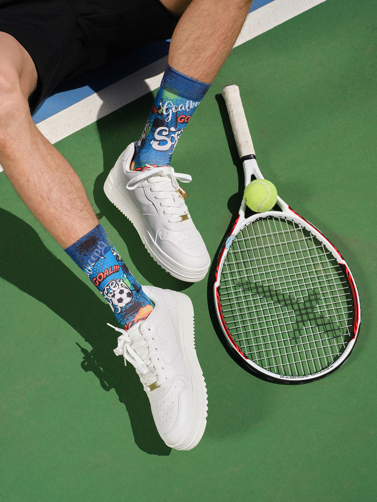 Person wearing white sneakers with colorful socks on a tennis court, holding a tennis racket and ball.