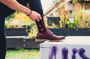Person wearing dark socks with colorful patterns and brown shoes, standing on a concrete block outdoors.