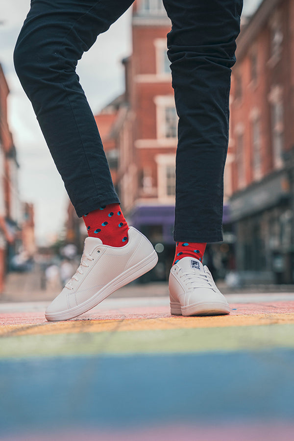 Person wearing white sneakers and red socks with black polka dots on a city street.