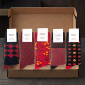 A gift box containing five pairs of IEMSOX socks in different patterns and colors, displayed on a dark wooden surface.