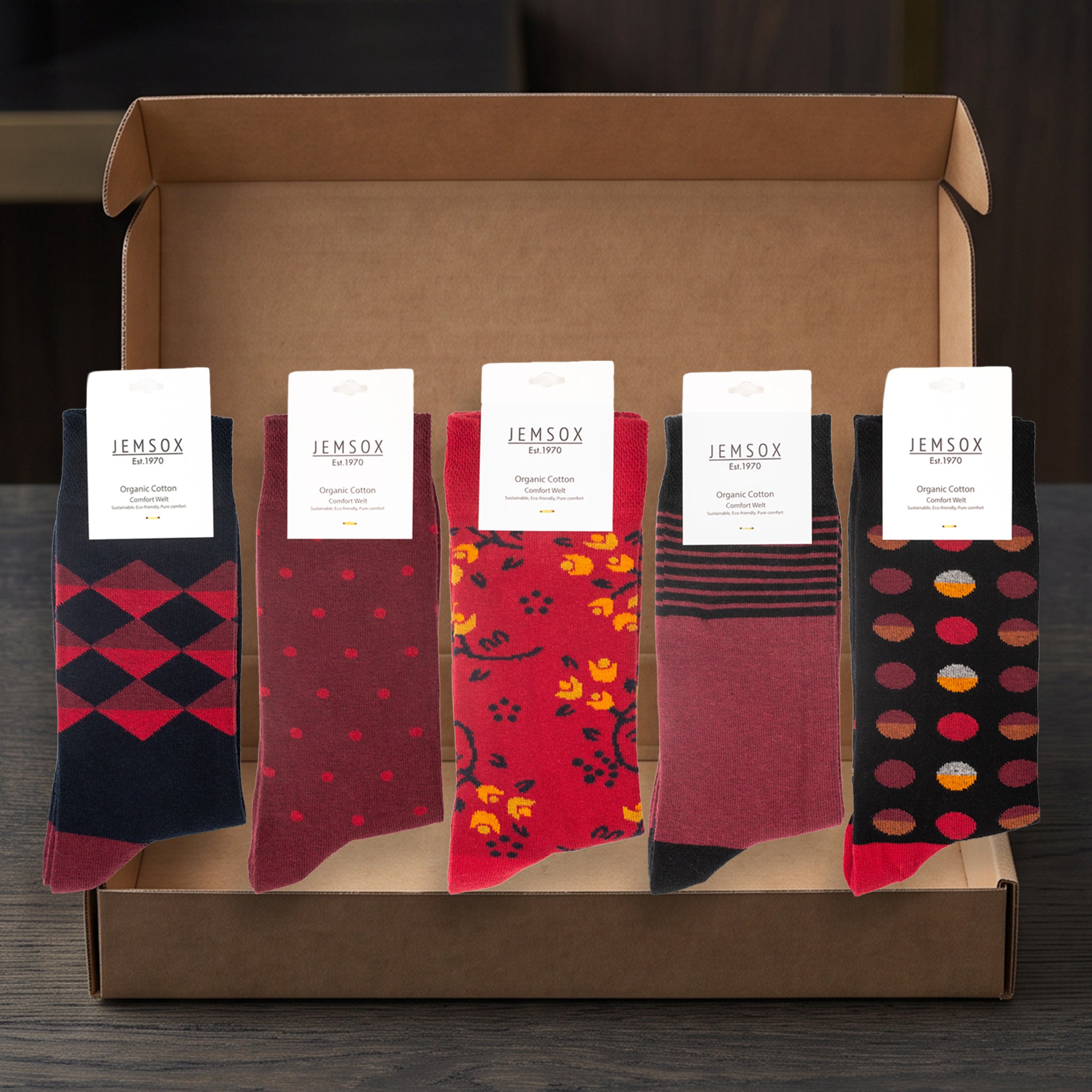 A gift box containing five pairs of IEMSOX socks in different patterns and colors, displayed on a dark wooden surface.