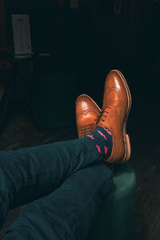 Brown dress shoes and blue pants with pink fox socks on a dark background