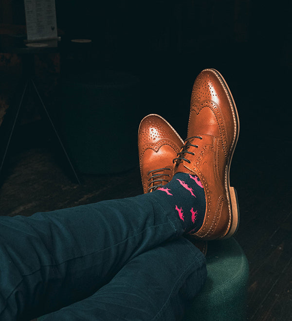 Brown dress shoes and blue pants with pink fox socks on a dark background