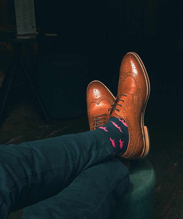 Brown dress shoes and blue pants with pink fox socks on a dark background