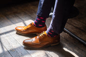 Brown leather shoes and fox patterned socks on a wooden floor