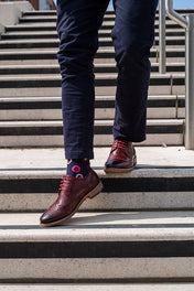 Person wearing navy chinos with navy pink socks and brown shoes on a set of concrete stairs.