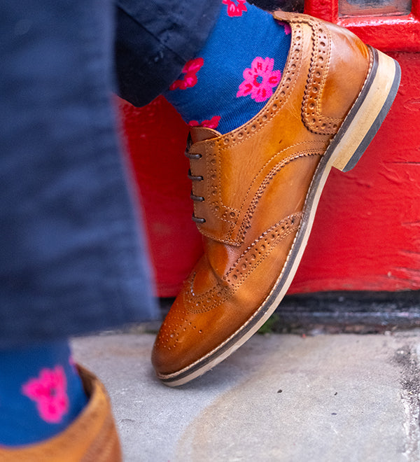 Brown leather shoes and blue socks with pink floral patterns on a red door background