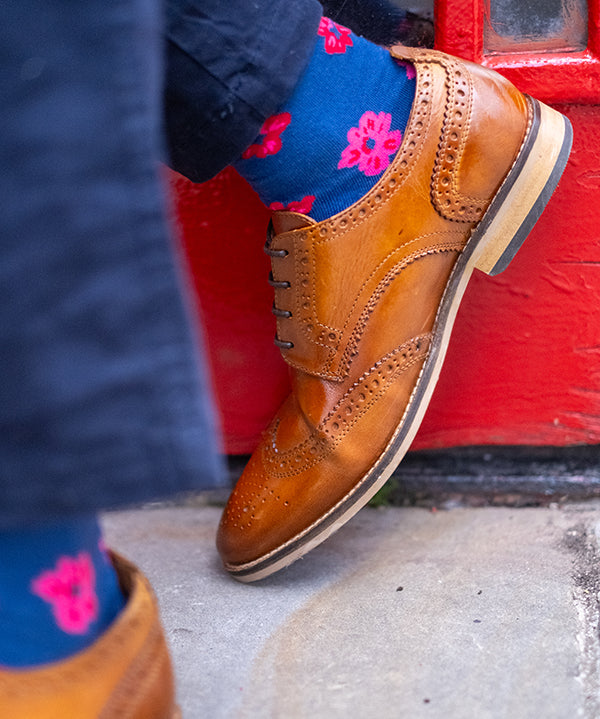 Brown leather shoes and blue socks with pink floral patterns on a red door background