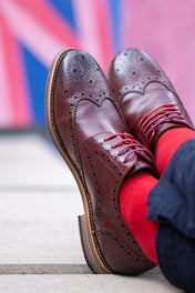 Brown leather shoes with red laces and red socks against a blurred background