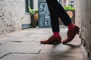 Person wearing brown shoes and red socks walking down a narrow alleyway.
