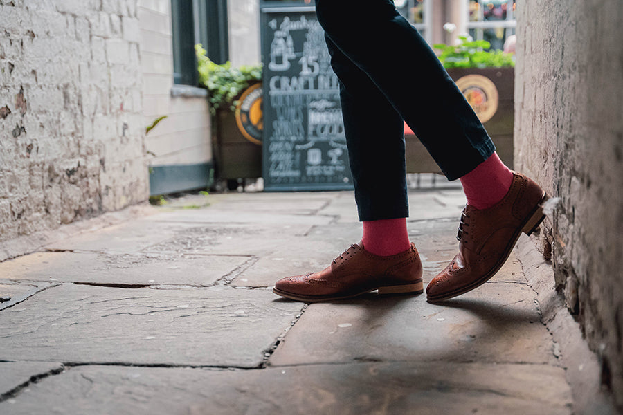 Person wearing brown shoes and red socks walking down a narrow alleyway.