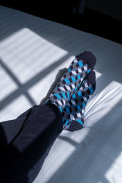 Person wearing patterned socks on a light-colored floor with shadows cast by a window.