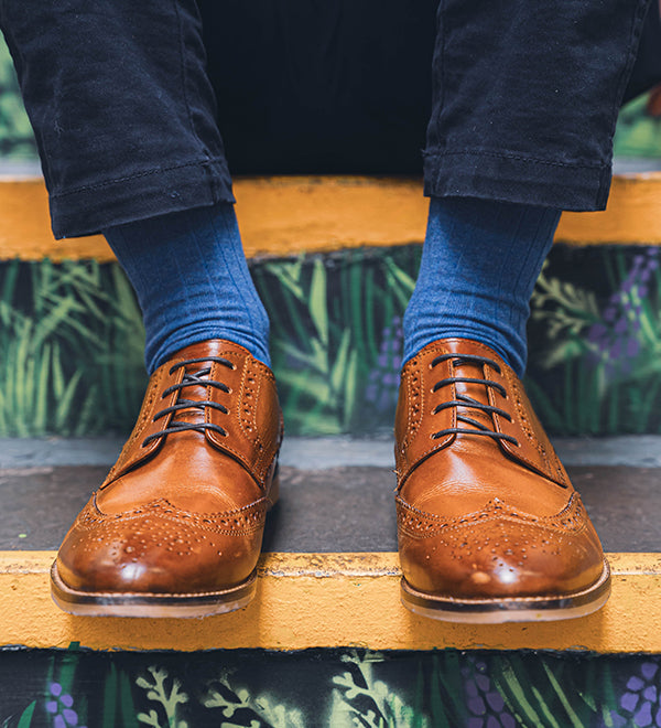 Person wearing brown leather shoes and blue socks on a decorative step.