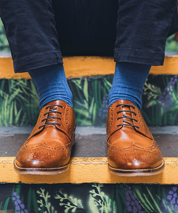 Person wearing brown leather shoes and blue socks on a decorative step.