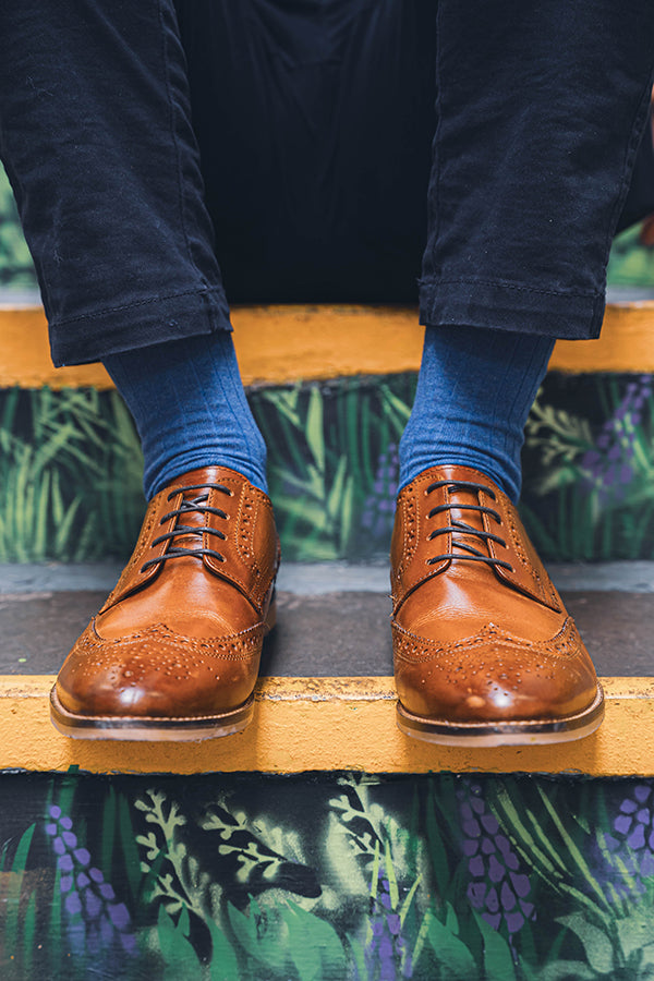 Person wearing brown leather shoes and blue socks on a decorative step.