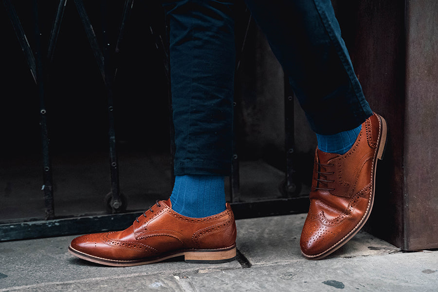 Brown leather shoes worn with blue socks on a dark background