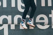 Person wearing striped socks and white sneakers with blue accents, standing on a street sign.