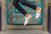 Person wearing white sneakers with blue swooshes and orange socks jumping in front of a textured wall.