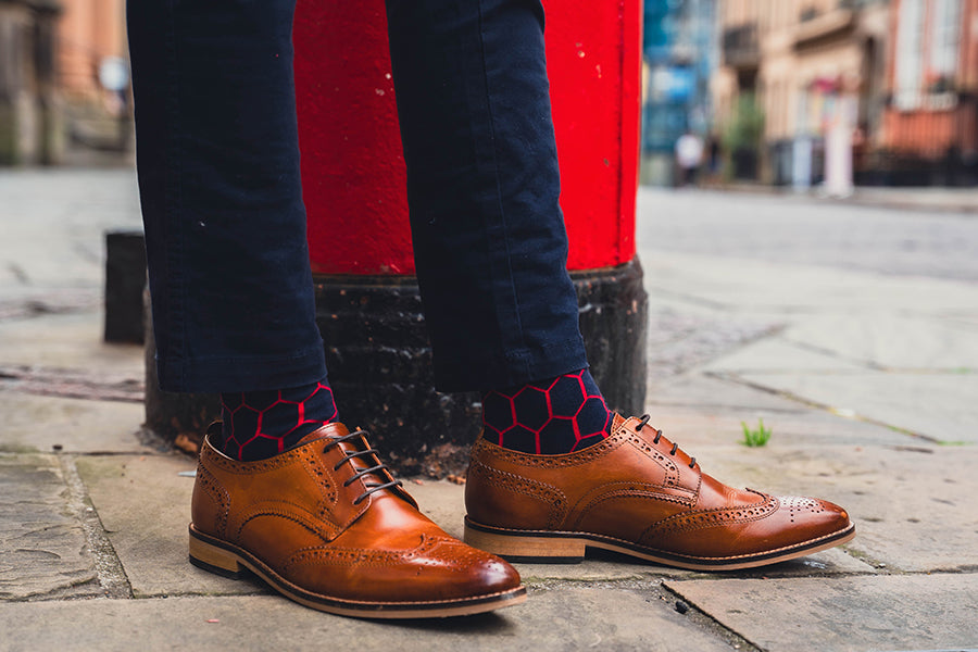 Brown leather shoes worn with cool navy patterned socks on a city street.