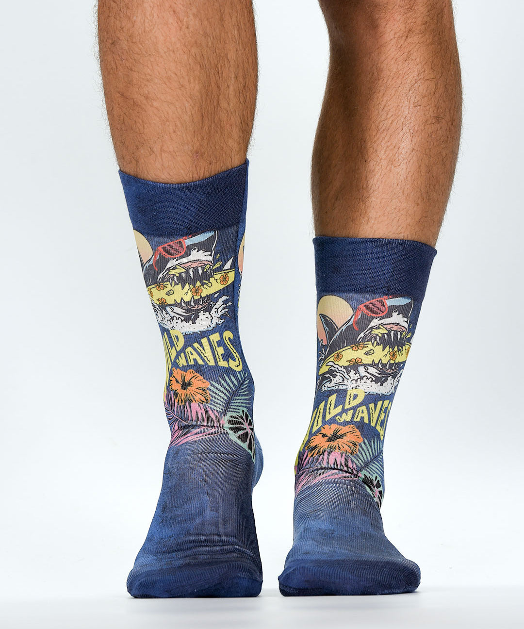 Colorful socks with shark design and 'WIld Waves' text worn by a person on a white background