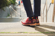 Person wearing red shoes and colorful cool socks standing on a sidewalk.