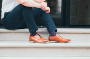 Person wearing brown shoes and funky patterned socks sitting on steps.