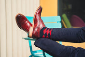 Person wearing red leather shoes and patterned socks sitting on a colorful chair.