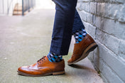 Person wearing brown shoes and checkered formal socks against a concrete wall.