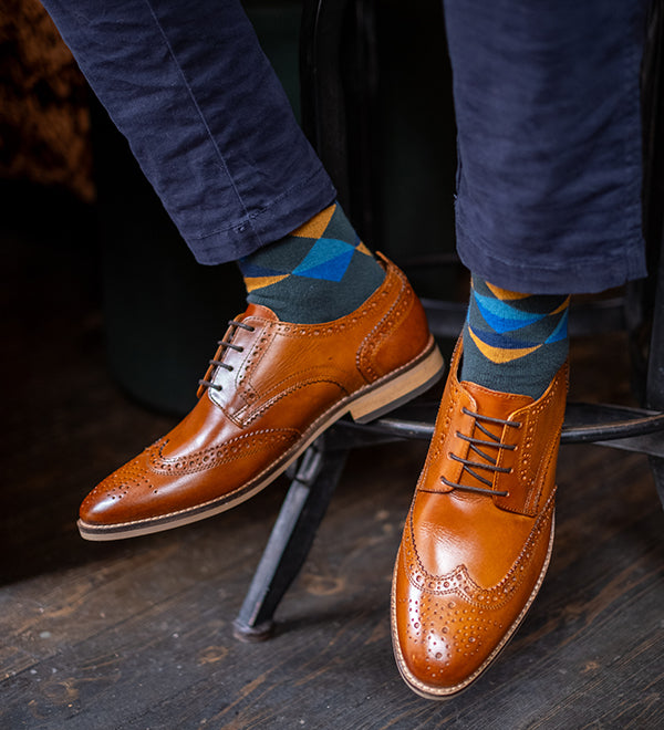 Brown leather shoes and blue jeans with mens green socks on a wooden floor.