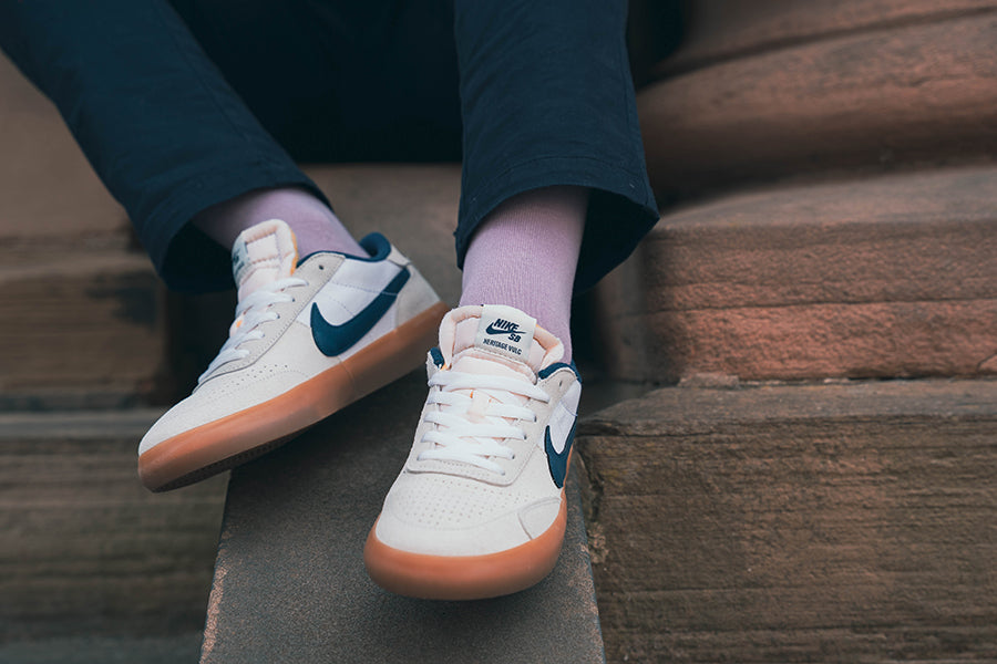 White sneakers with purple socks worn on a person sitting on steps.