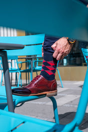 Person wearing red and blue patterned socks with brown shoes on a blue chair.