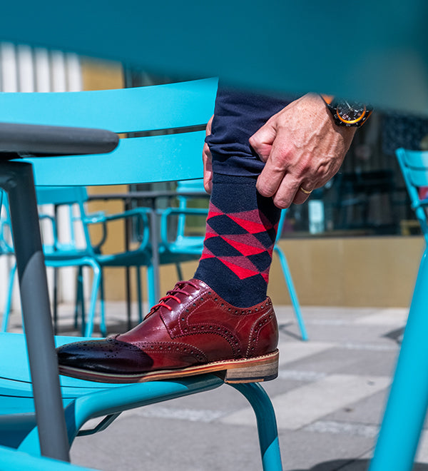 Person wearing red and blue patterned socks with brown shoes on a blue chair.