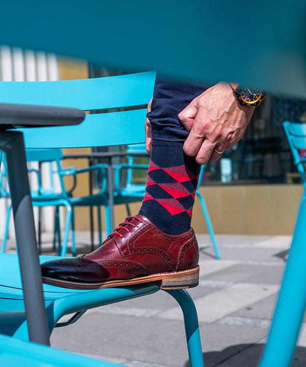 Person wearing red and blue patterned socks with brown shoes on a blue chair.