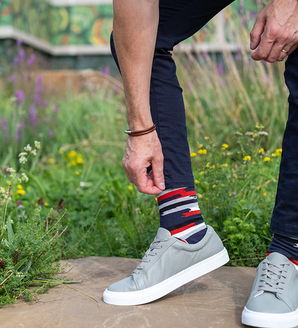 Person wearing gray sneakers and colorful socks standing on a stone surface with a natural background.