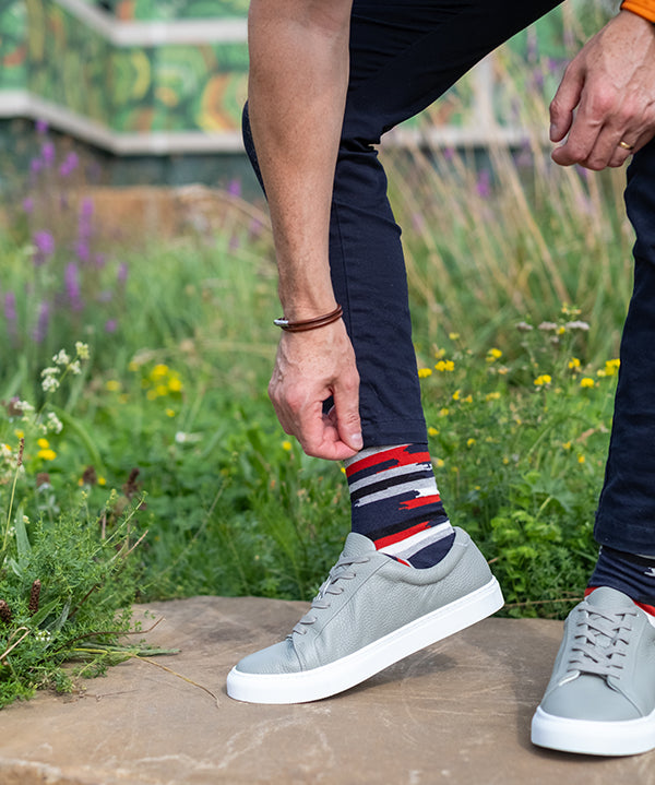 Person wearing gray sneakers and colorful socks standing on a stone surface with a natural background.