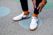 Person wearing white sneakers with blue swooshes, orange socks, and black levi jeans on a concrete surface.