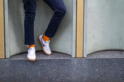 Person wearing navy pants, white sneakers with orange socks, standing on a ledge.