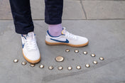 White sneakers with blue accents on a concrete surface with small round objects.