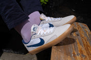 White sneakers with purple socks worn by a person sitting on a wooden bench.