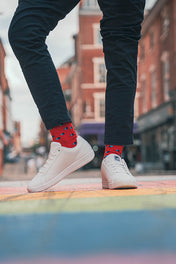 Person wearing white sneakers and red socks with black polka dots on a city street.