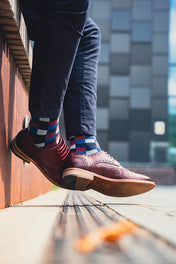 Person wearing brown shoes and patterned socks standing on a wooden floor with a blurred background.