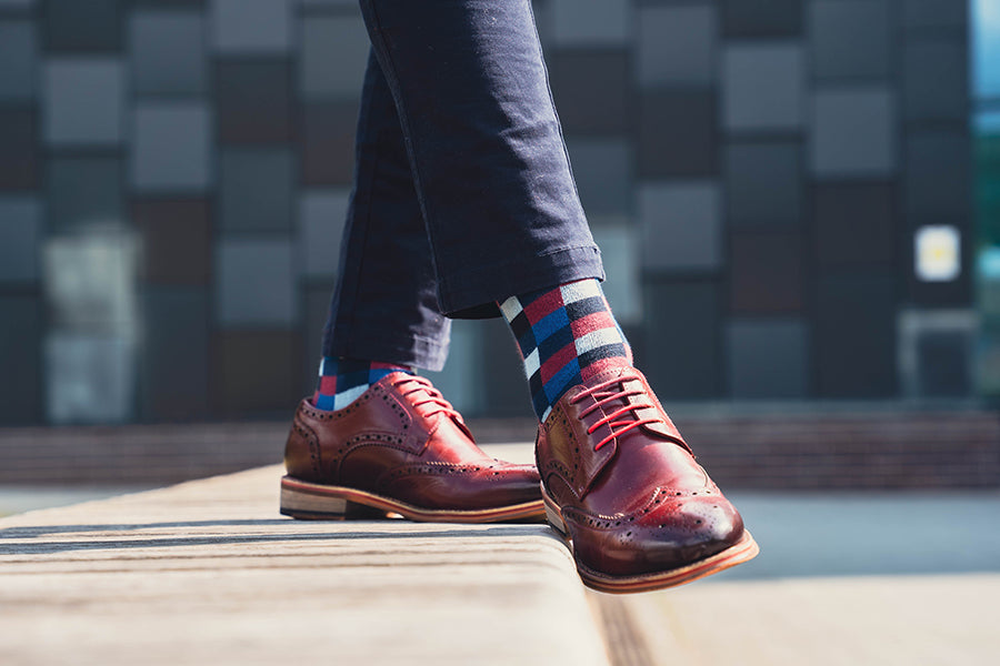 Person wearing brown leather shoes and colorful socks on a blurred background
