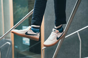 Person wearing white sneakers with striped socks, standing on a metal railing.