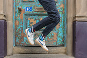 Person in blue jeans, varsity striped socks and white sneakers jumping in front of a textured door with peeling paint.