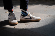 White sneakers with black Nike logo combined with bold stripe socks worn on a sidewalk